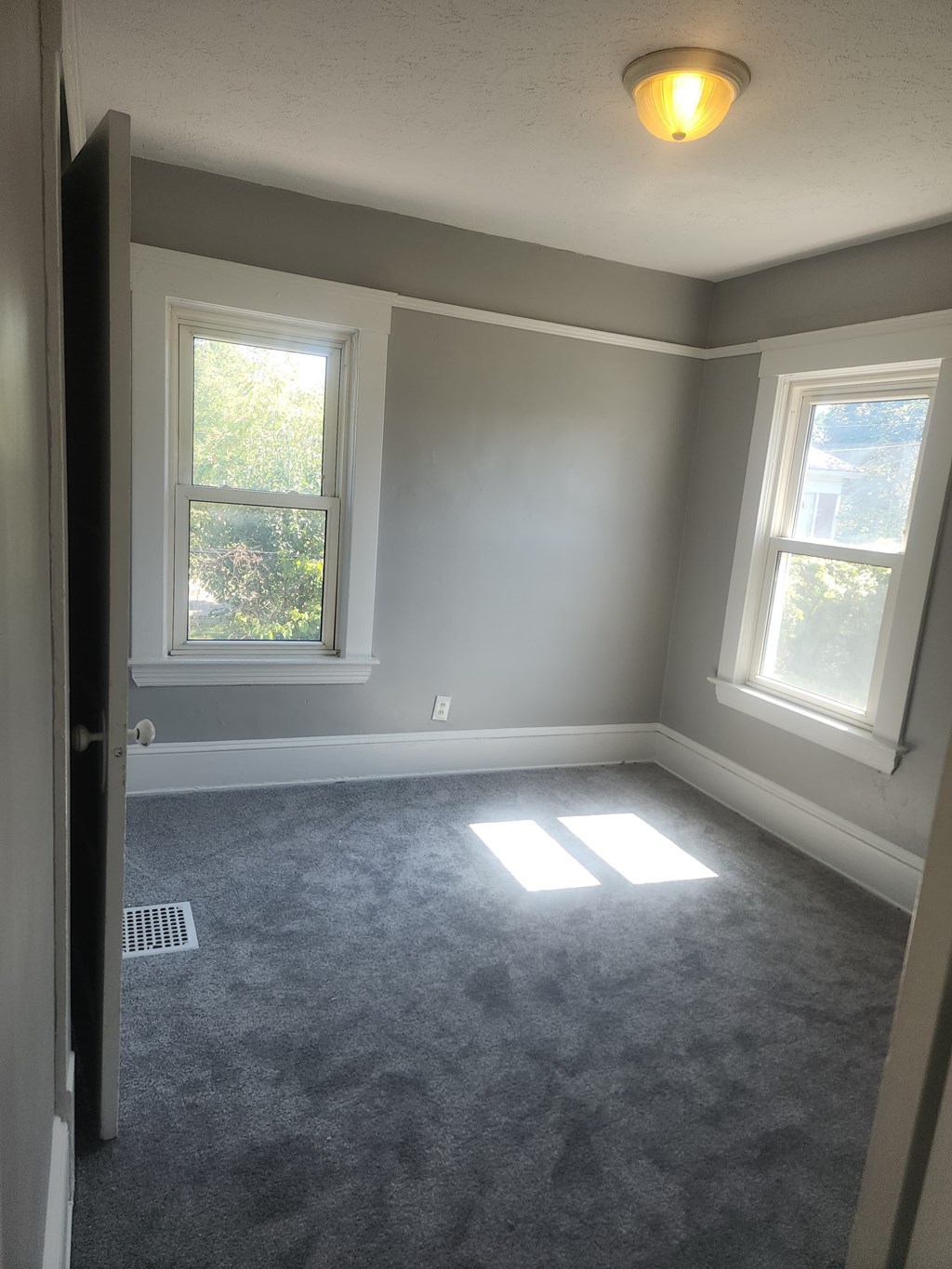 A room with grey carpet and two windows.