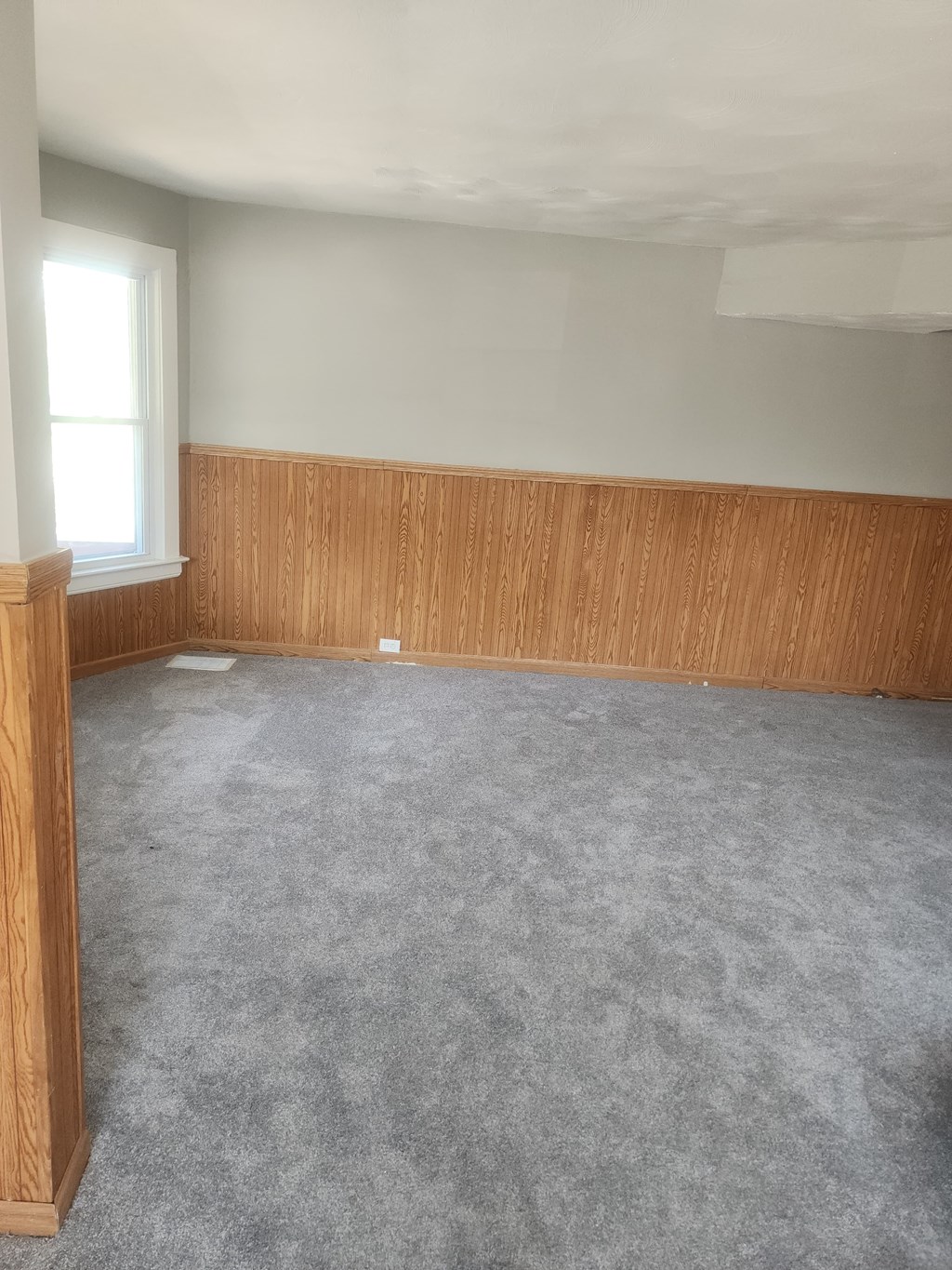 A room with a grey carpet and wooden paneling on the walls.