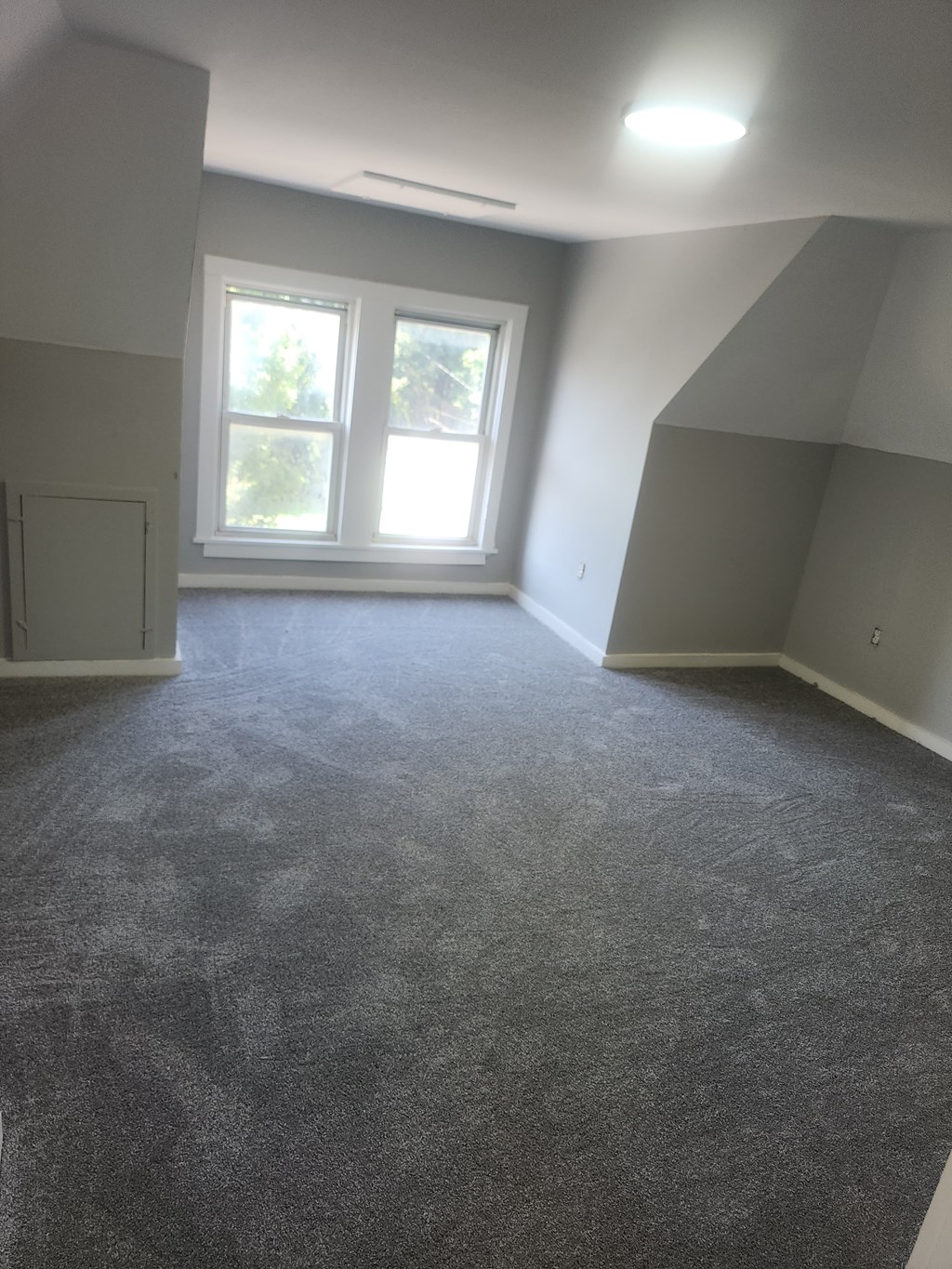 A room with grey carpet and a window.