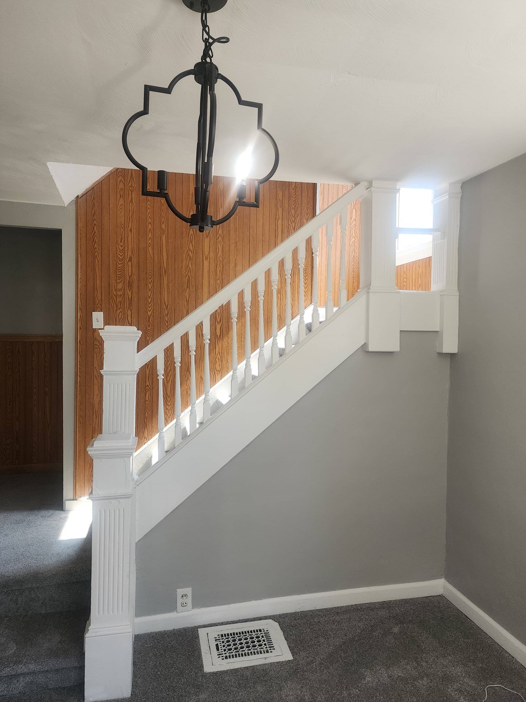 A chandelier hangs over a staircase with a white railing.