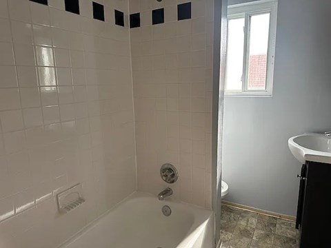 A white tiled bathroom with a tub, shower, and a window.