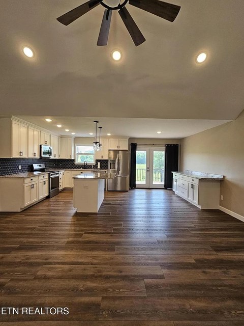 A spacious kitchen with a fan and wooden flooring.