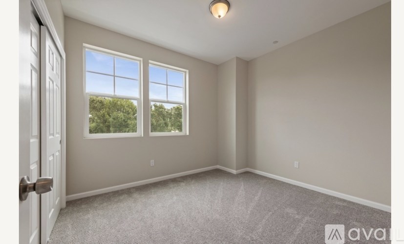 A room with a carpeted floor, a door, and a window with a view of trees outside.