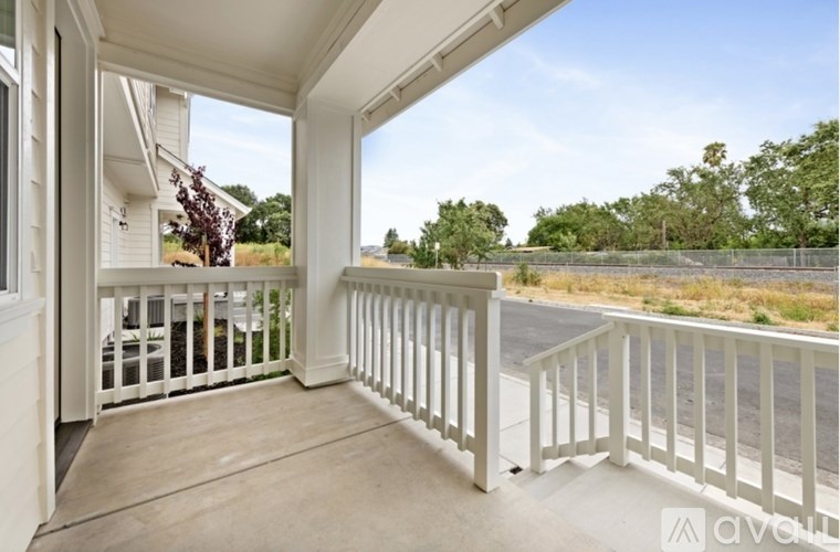 A balcony with white railings and a view of a road and trees.