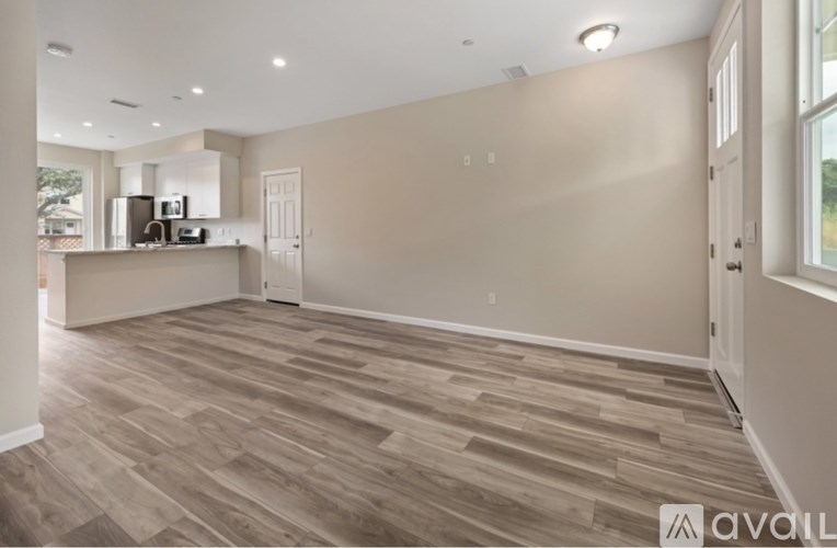 A spacious room with wooden flooring and a kitchen area in the background.