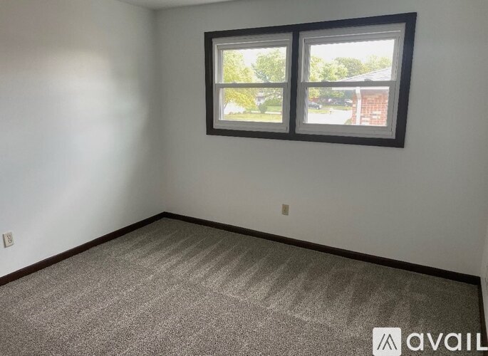 A room with a carpeted floor and a window showing a view of a house.