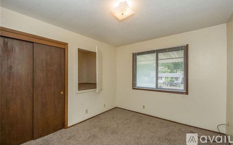 A room with a brown door, a window with blinds, and a carpeted floor.