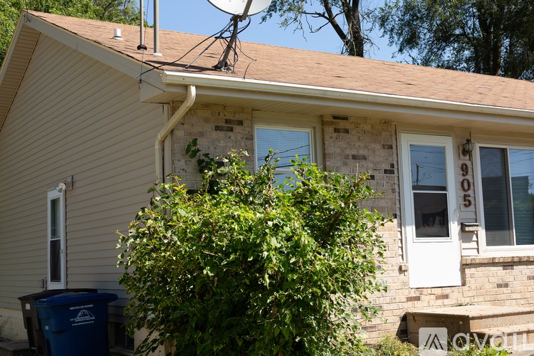 A house with a blue trash bin in front of it.