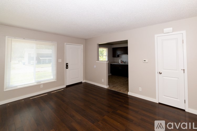 A room with wooden floors and white walls, with a door leading to another room visible in the background.