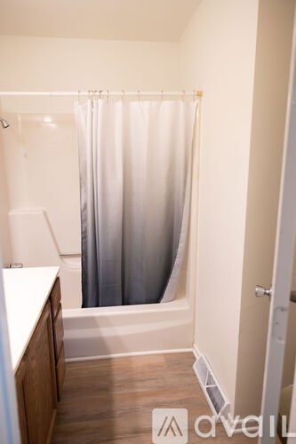 A white bathroom with a shower curtain and wooden floors.