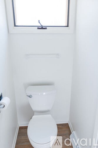 A white toilet in a small bathroom with a window above it.