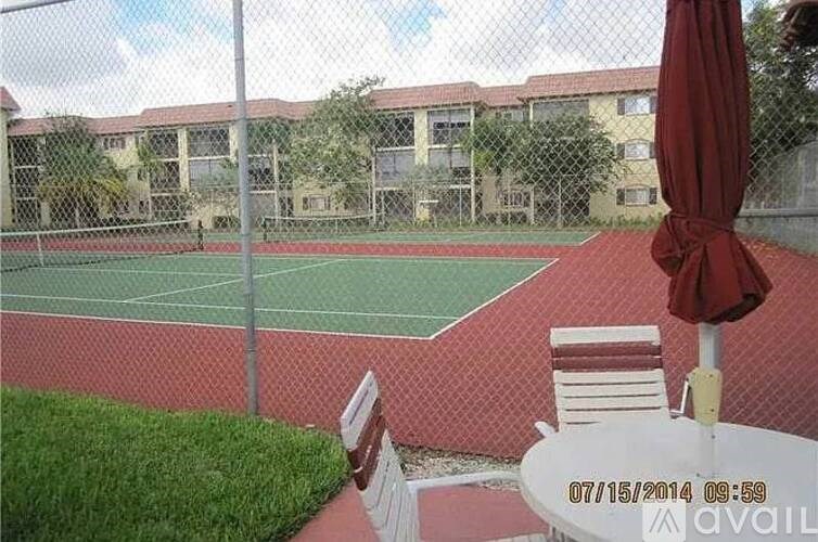 A tennis court with a red umbrella and two chairs.