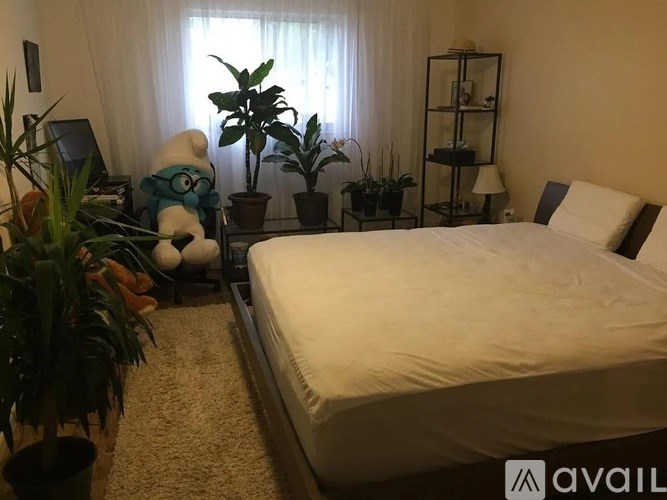 A bedroom with a bed, a nightstand, a lamp, a plant, and a stuffed animal.