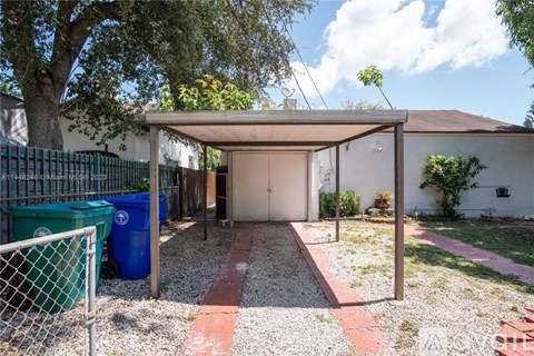 A backyard with a gravel pathway, a green trash can, and a blue trash bin.