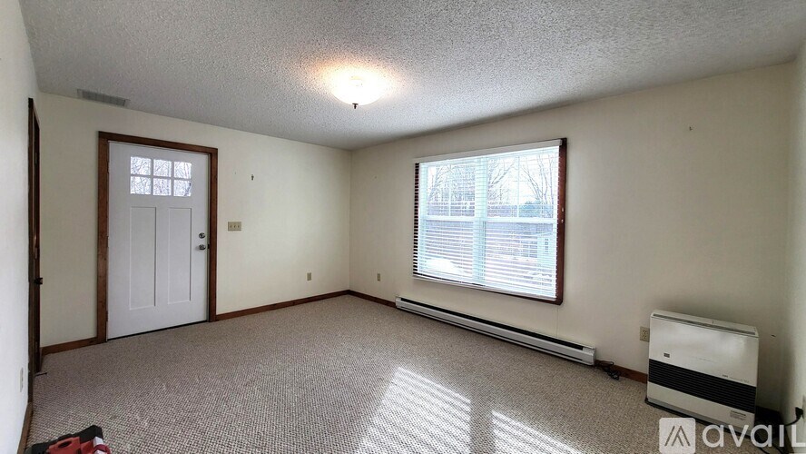 A room with a carpeted floor, a window with blinds, and a door.