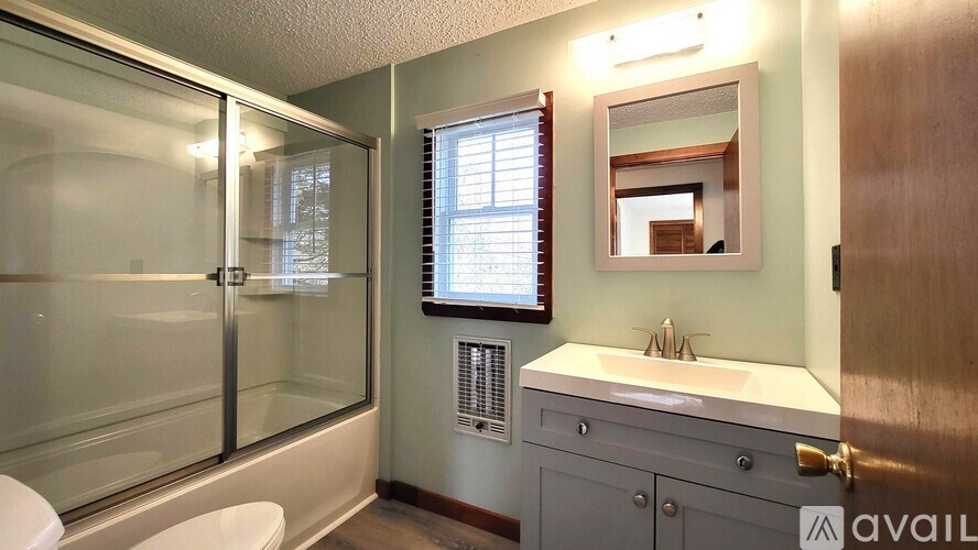 A bathroom with a glass shower stall, sink, and mirror.