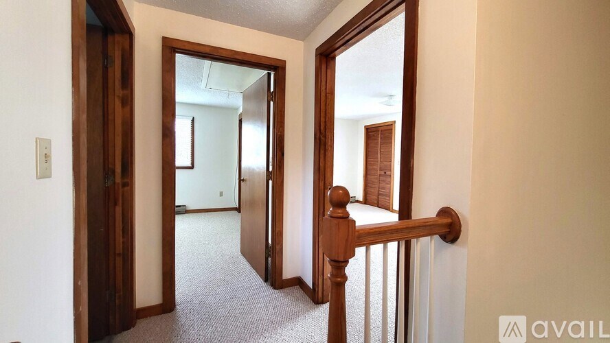 A hallway with a carpeted floor, a wooden door, and a wooden railing.
