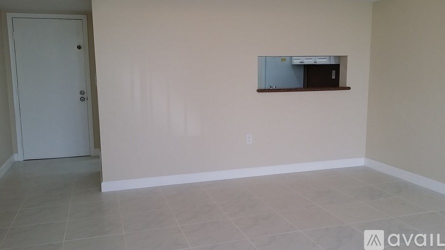 A room with a white door and a window with a view of a kitchen.