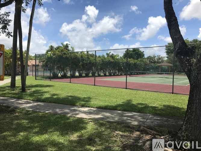 A tennis court is surrounded by a fence and trees.