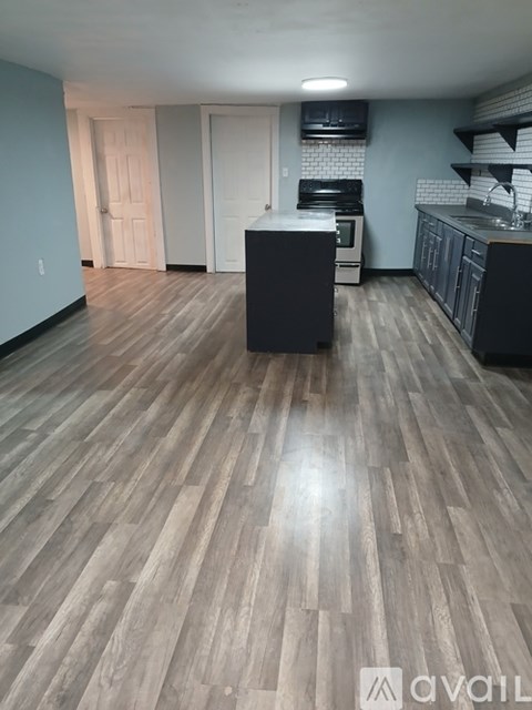 A kitchen with wooden flooring and a black island in the middle.