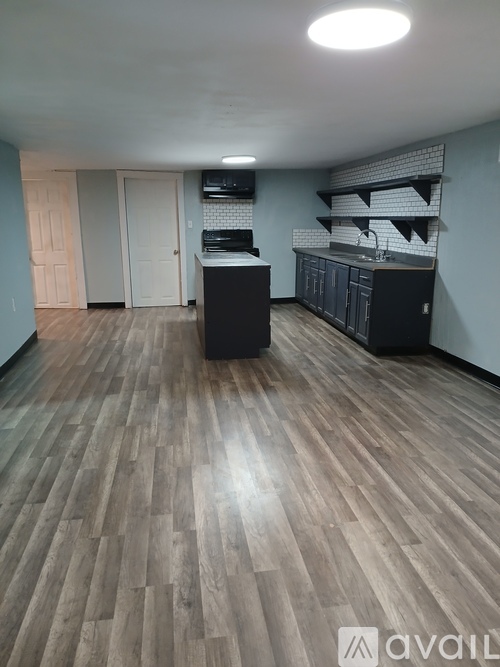 A room with wooden flooring and a kitchenette in the background.