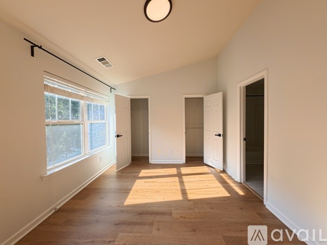 A room with wooden flooring and white walls, with a window on the left side.