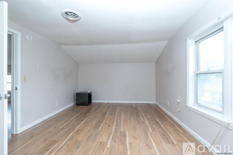 A room with wooden floors and a window on the right side.