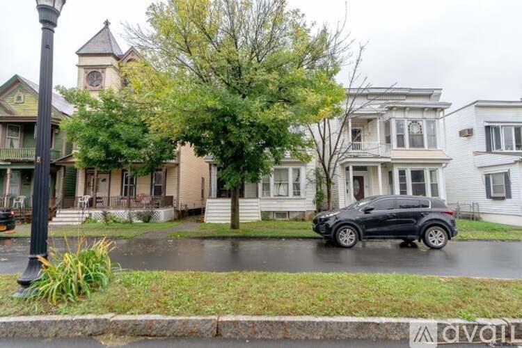 A black car is parked on a wet street in front of a house.
