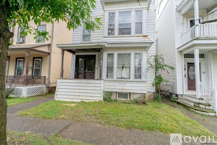 A white house with a balcony and a tree in front.