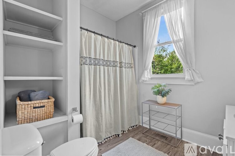 A bathroom with a toilet, a basket, a towel, a shower curtain, a window, and a plant.