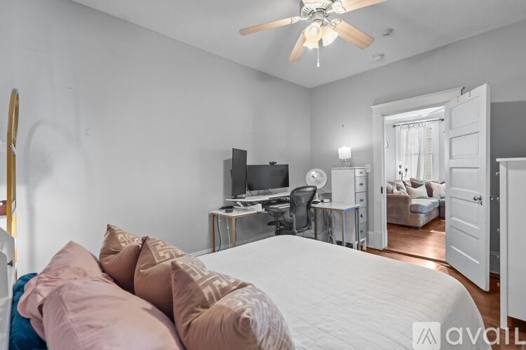 A bedroom with a bed, a desk, and a ceiling fan.