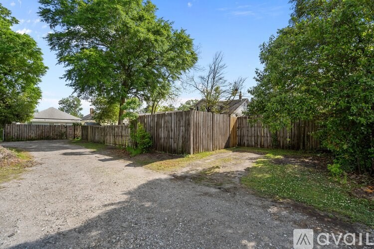 A gravel driveway leads to a wooden fence with green trees on either side.