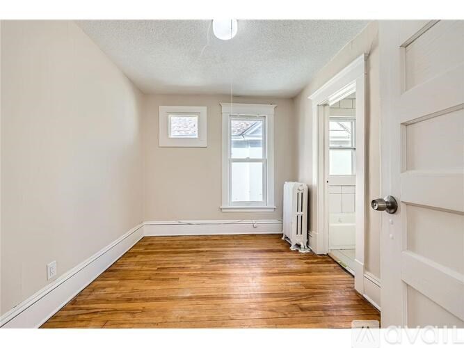 A room with wooden floors and white walls, with a window and a door visible.