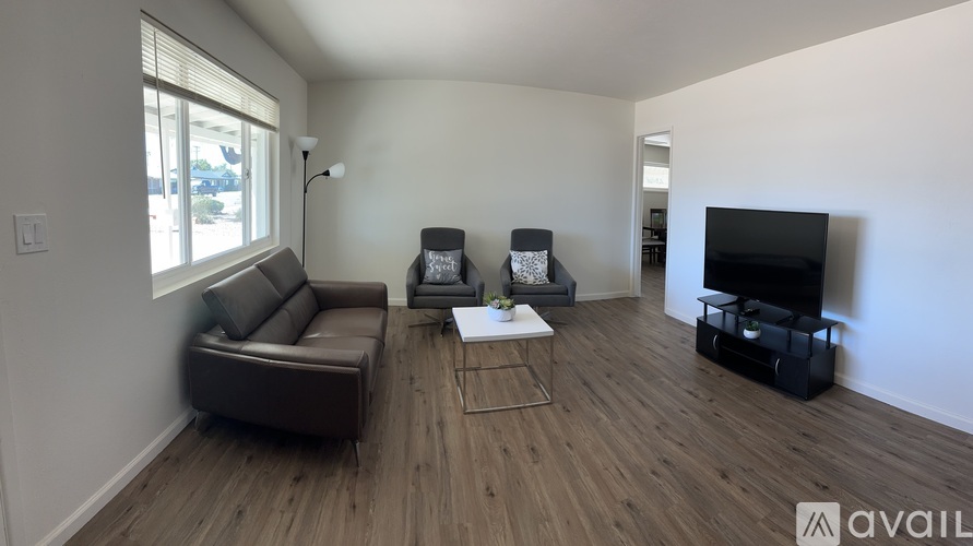 A living room with a brown leather couch, a white coffee table, and a black television.