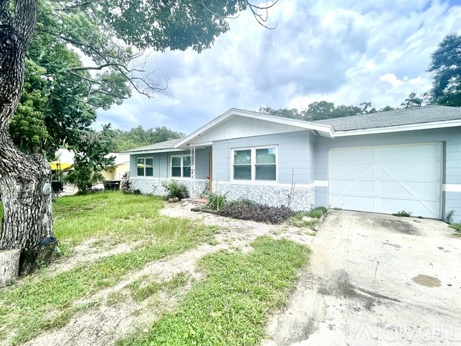A house with a white garage door is surrounded by greenery.