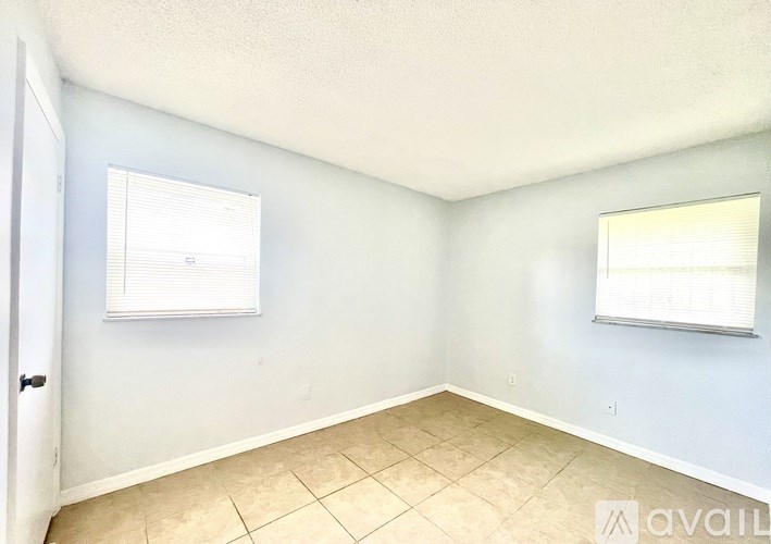 A room with a tiled floor and two windows with blinds.