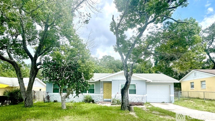 A white house with a yellow garage door is surrounded by trees.