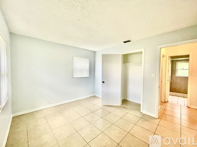 A room with a white door, a window with blinds, and a tiled floor.