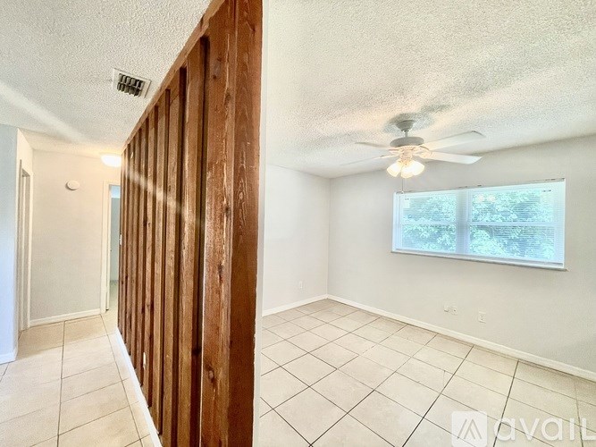 A room with a ceiling fan and a window with a view of trees.