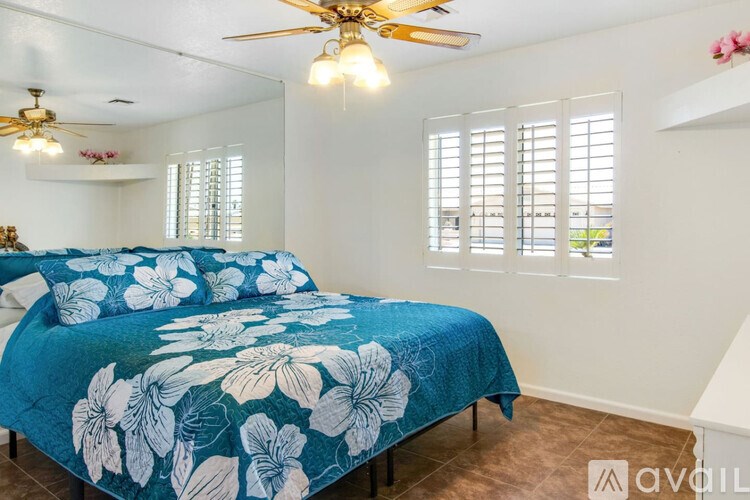 A bedroom with a blue floral bedspread and a ceiling fan.