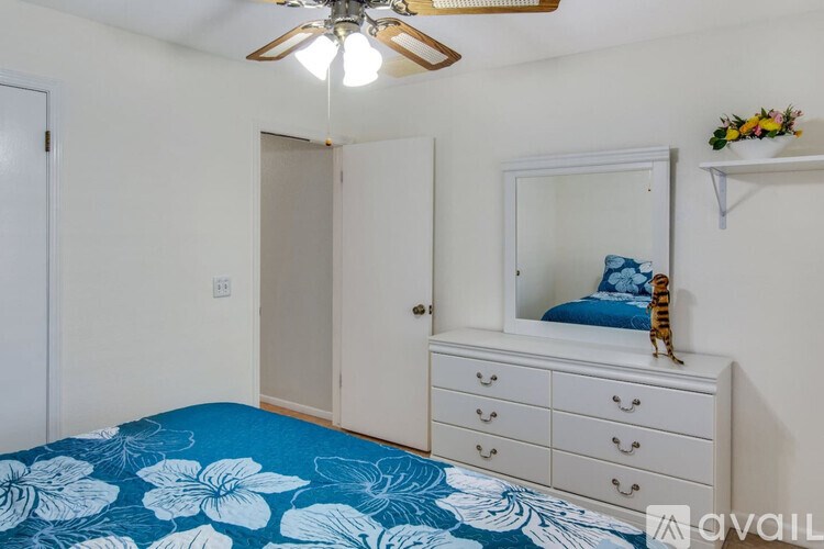 A bedroom with a blue floral bedspread and a white dresser with a mirror above it.