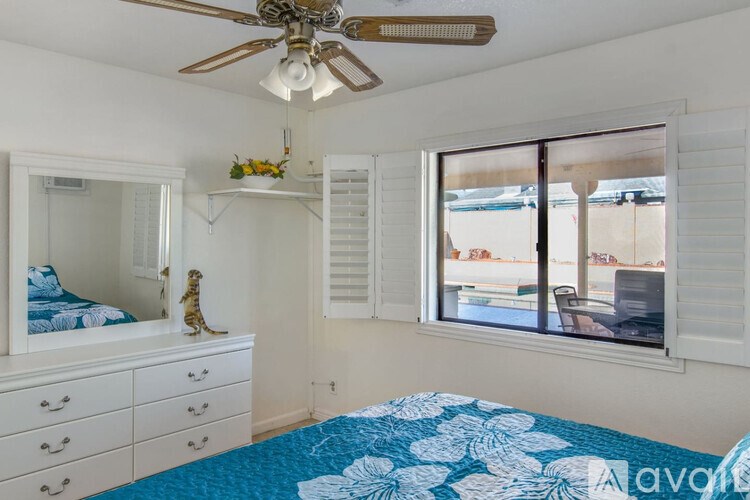 A bedroom with a blue and white bedspread and a ceiling fan.