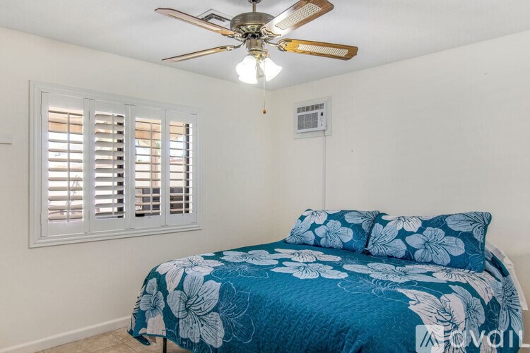 A bedroom with a blue floral bedspread and a ceiling fan.