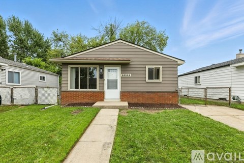 A small house with a white door and windows is surrounded by a fence and green grass.