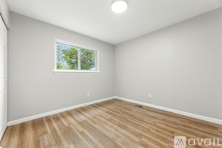 A room with wooden flooring and a window showing trees outside.