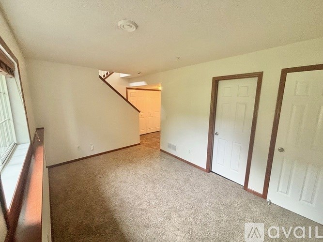 A room with white walls and carpeted floor with a staircase in the background.