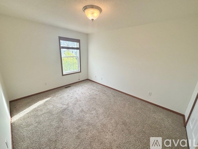 A room with a carpeted floor and a window showing a view of a garden outside.