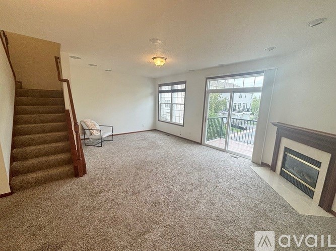 A living room with a carpeted floor, a staircase, a fireplace, and a sliding glass door.