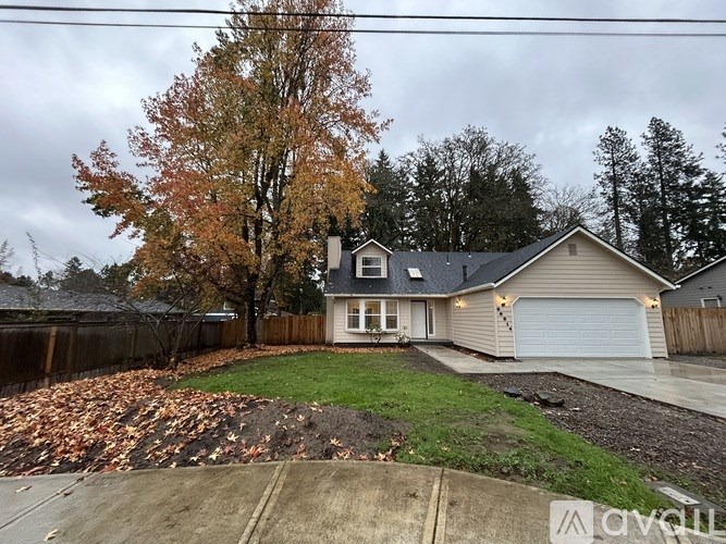A house with a garage and a tree with orange leaves in front of it.