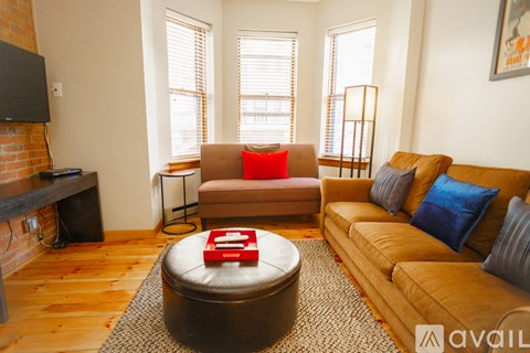 A living room with a brown couch, a red ottoman, and a television.
